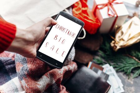 christmas big sale. special christmas offer discount text on phone screen message on seasonal rustic background with money cards wallet and bag with stuff and presents. advertising conceptの写真素材