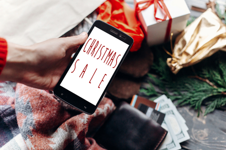 christmas big sale. special christmas offer discount text on phone screen message on seasonal rustic background with money cards wallet and bag with stuff and presents. advertising conceptの写真素材