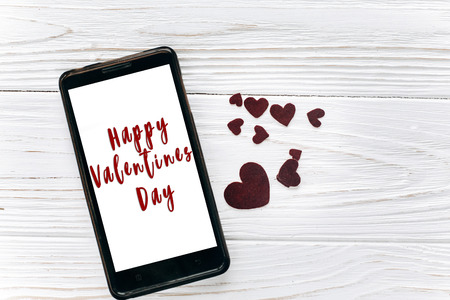 happy valentines day text sign on smart phone with empty screen and hearts flat lay on white background, space for text.  greeting card. communication and waiting a messageの写真素材