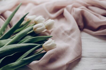 stylish white tulips on beige soft fabric and rustic wooden table background. hello spring. soft light, tenderness atmospheric moment. space for text. rustic weddingの写真素材