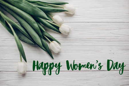 happy women's day text sign. hello spring flat lay. stylish white tulips on rustic wooden table background top view. soft light, tenderness atmospheric moment.の写真素材