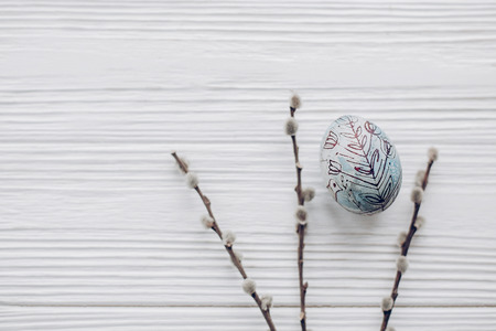 simple easter egg with floral ornaments and willow buds on rustic white wooden desk background....