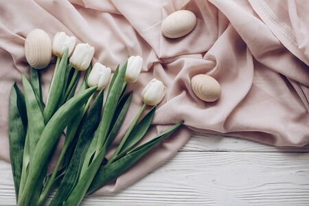 happy easter concept. stylish white tulips and simple easter eggs on rustic wooden background and fabric flat lay. greeting card with space for text, top view. soft lightの写真素材