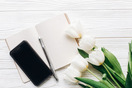 phone screen and notebook pen and stylish tulips on white wooden rustic background. flat lay with flowers and paper note with space for text. happy mothers womens day conceptの写真素材