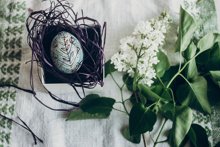 happy easter. easter egg in nest with floral and chick ornaments on rustic background with lilac flowers. top view. space for text.  greeting card concept. stylish decorationの写真素材