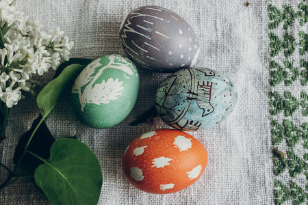 easter eggs with floral and chick ornaments on rustic background with lilac flowers. top view. space...
