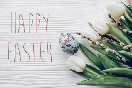 happy easter text greeting card sign on stylish easter egg and willow buds and white tulips on...