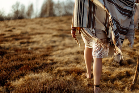 woman legs in native indian american boho dress walking in windy sunny evening mountains, holding feathersの写真素材