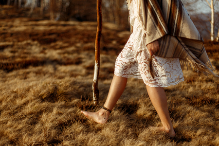 woman legs in native indian american boho dress walking in windy sunny evening mountains, holding feathersの写真素材