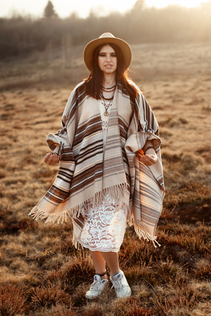 beautiful woman hipster posing, wearing hat and poncho,  at sunset in mountainsの写真素材