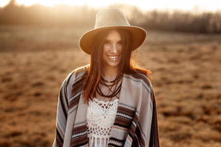 beautiful boho woman hipster, smiling, wearing hat and poncho at sunset in mountains, true emotions, space for textの写真素材