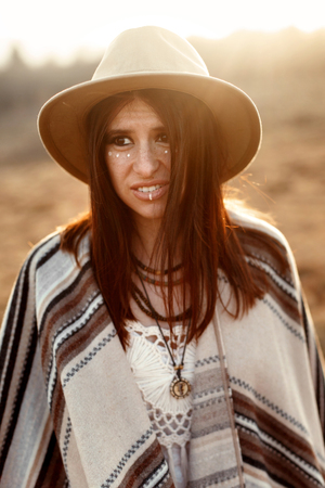 beautiful boho woman hipster portrait, wearing hat and poncho,  at sunset in mountains,  funny  lookの写真素材