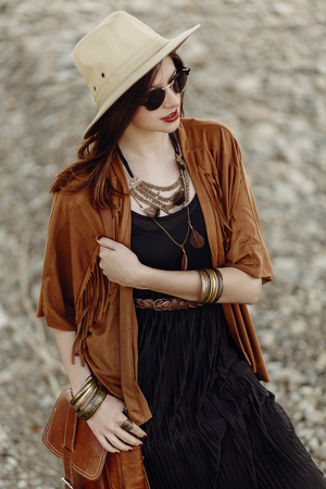 beautiful stylish boho woman in sunglasses and hat, fringe poncho and leather bag. hipster girl in...