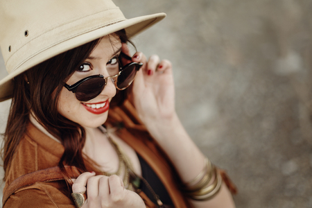 beautiful stylish hipster woman in sunglasses smiling, looking up, with windy hair. boho traveler girl in gypsy look, near beach in mountains. atmospheric moment.  space for text.の写真素材