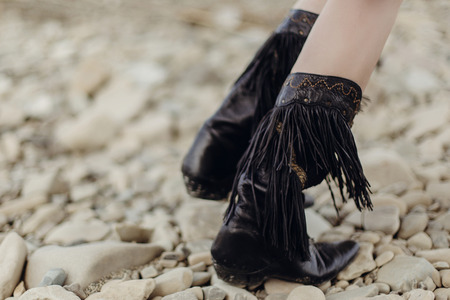 boho girl walking in fringe boot. stylish hipster traveler woman wearing suede boots on river beach. gypsy look. wanderlust summer travel. atmospheric moment. space for text.の写真素材