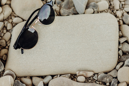wanderlust and travel concept. stylish hipster sunglasses on beach top view with space for text. summer vacation and adventure. modern black glasses on stonesの写真素材