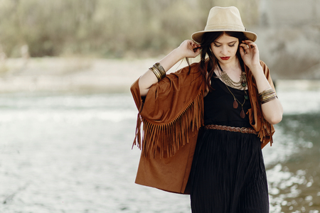 stylish hipster gypsy boho woman posing in hat with windy hair, in fringe poncho and accessory.  traveler girl look. summer travel. atmospheric moment. space for text. sensual portraitの写真素材