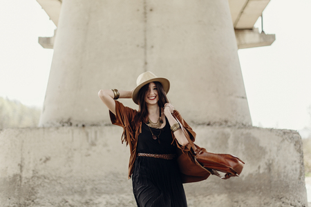 stylish hipster woman having fun and smiling, in hat with windy hair near river stones. boho traveler girl in gypsy look. summer travel. atmospheric moment. space for text.の写真素材