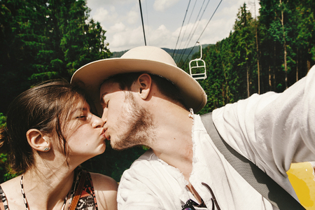 stylish hipster couple kissing on chairlift  in summer mountains, travel together conceptの写真素材