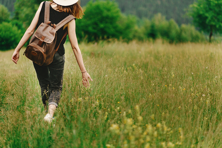 stylish hipster woman walking in grass and holding  in hand herb  wildflowers  in summer mountains, travel concept, peaceful relaxing momentの写真素材