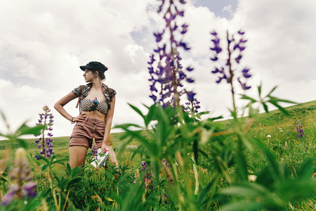 stylish hipster woman traveler standing among wildflowers and  lupin in mountains, travel and summer adventure concept, unusual viewの写真素材