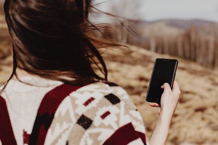 happy stylish woman hipster holding phone with empty screen  in summer mountainsの写真素材