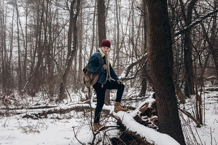 stylish hipster traveler with backpack posing in winter snowy forest trees. wanderlust and adventure concept with space for text. atmospheric momentの写真素材
