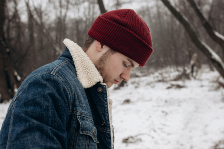 stylish hipster traveler with backpack in red hat  walking in winter snowy forest. wanderlust and...