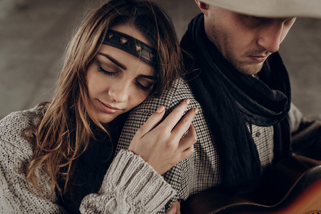 Romantic brunette hipster girl in boho clothes hugging handsome cowboy musician with guitar and a scarf closeupの写真素材