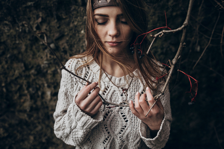 stylish hipster woman posing in knitted sweater holding branch with berries. atmospheric sensual moment. boho country fashionable look.の写真素材