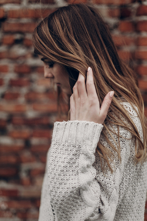 Beautiful brunette hipster woman in white boho sweater, face closeup, brick wall backgroundの写真素材