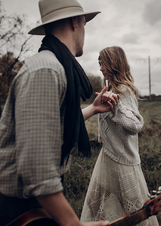 stylish hipster couple holding sensually hands. boho gypsy woman and man in hat embracing in windy field. atmospheric amazing moment. fashionable look. rustic wedding conceptの写真素材