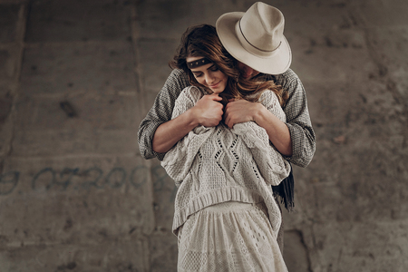 Handsome stylish cowboy man in hat and shirt embracing beautiful gypsu woman from behind, sensual couple smilingの写真素材