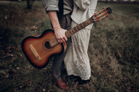 stylish hipster couple posing in windy field. boho gypsy woman and man with guitar in windy field. atmospheric motion moment. fashionable look. rustic wedding conceptの写真素材