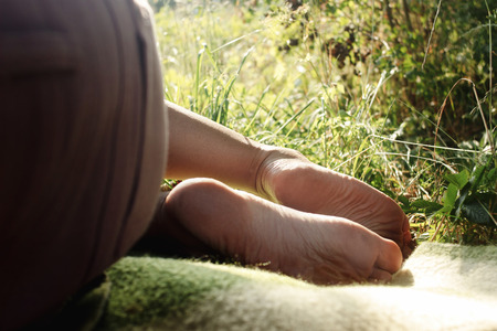 woman legs barefoot on blanket on a picnic in a garden under warn sunshine, summer relaxationの写真素材