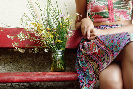 woman sitting on old wooden red bench with  rustic bouquet of wild flowers at country house, summer vacationの写真素材