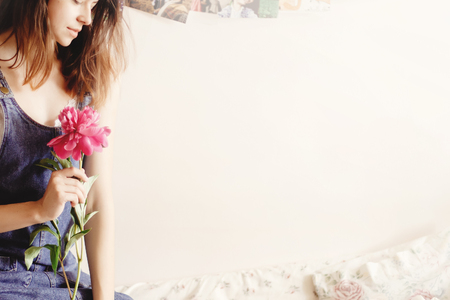 woman hipster  holding peony and sitting on bed in the morning, sweet romantic moment, space for textの写真素材