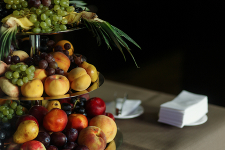 Delicious, healthy fruit tower at wedding reception dessert table close-up, brown tablecloth background, peaches, grapes, pineapple and pear meal at wedding cateringの写真素材