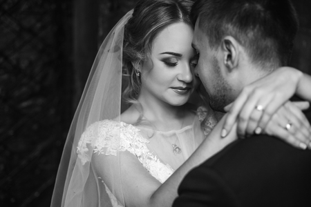Happy newlywed couple portrait, face closeup of newlywed blonde bride hugging smiling groom near old metal gate, emotional couple on honeymoonの写真素材