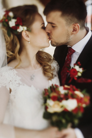 Portrait of  romantic newlywed couple, handsome groom kissing beautiful bride in vintage white wedding dress with roses bouquet, husband and wife posing outdoorsの写真素材