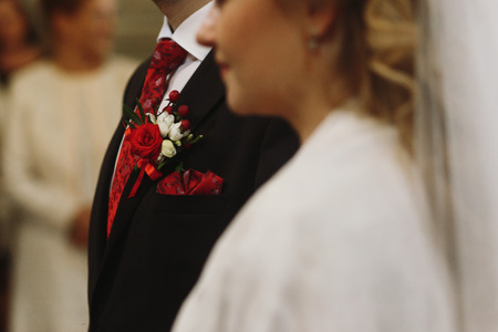Closeup of red rose boutonniere on groom's suit during wedding ceremony in church, red flower boutonniere on black jacketの写真素材