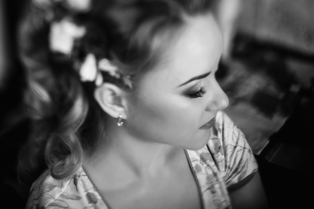 Beautiful bride putting on floral head wreath, stylist doing hairstyle for blonde woman in stylish robe, morning wedding preparation face closeupの写真素材