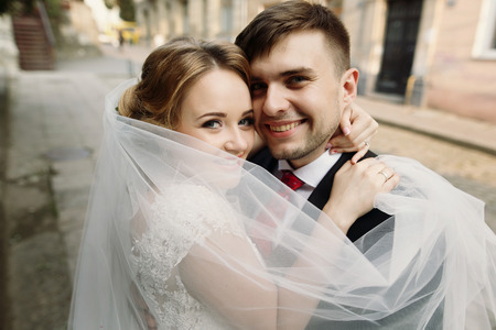 Cheerful bride and groom hugging face closeup, newlywed couple smiling in embrace outdoors, family portrait conceptの写真素材