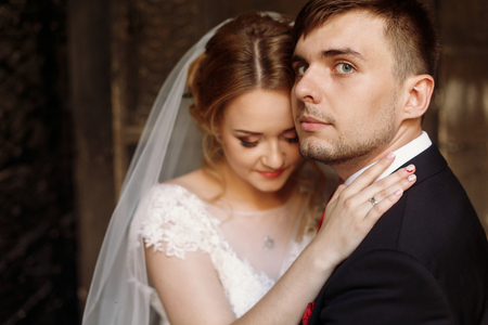 Happy newlywed couple portrait, face closeup of newlywed blonde bride hugging smiling groom near old metal gate, emotional couple on honeymoonの写真素材