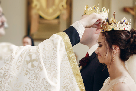 Sensual happy bride and groom wearing gold crowns during wedding ceremony in christian church,...