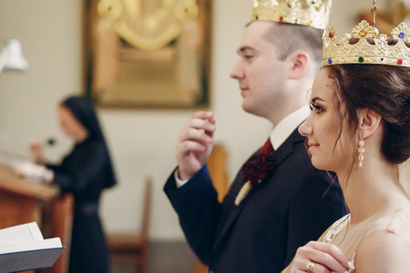 Sensual happy bride and groom wearing gold crowns during wedding ceremony in christian church, coronation ritual indoors face close-up, marriage conceptの写真素材