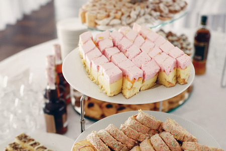 Delicious cakes with pink cream frosting and brown desserts at candy bar table at wedding reception...