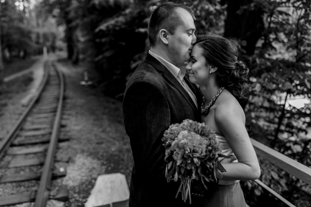 Happy newlywed couple kissing in a park near railroad, smiling groom with beautiful bride with bouquet hug near old railway, travel honeymoon conceptの写真素材