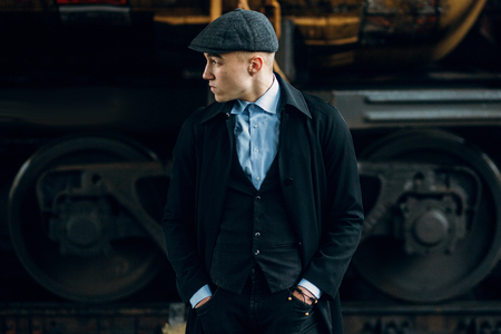 stylish gangster in retro outfit posing on background of railway. england in 1920s theme. fashionable look of brutal confident man. atmospheric moments. space for textの写真素材