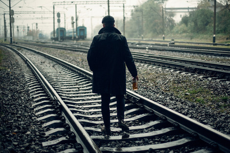 silhouette of stylish gangster man with bottle whiskey walking on railway road. england in 1920s theme. fashionable brutal confident man. atmospheric momentsの写真素材
